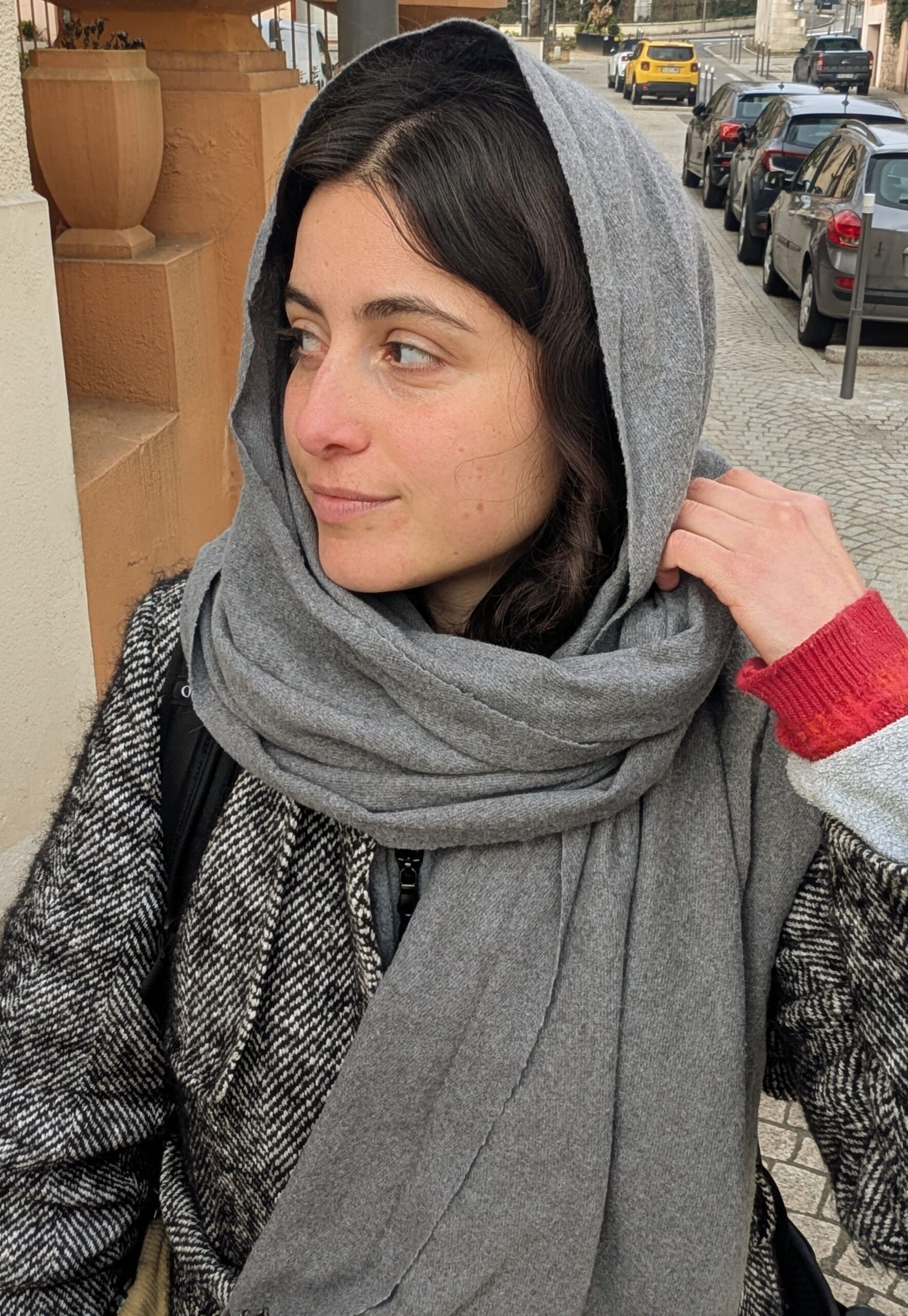 Sara portant un châle sur la tête ; les cheveux dépassent légèrement. Elle regarde sur le côté.