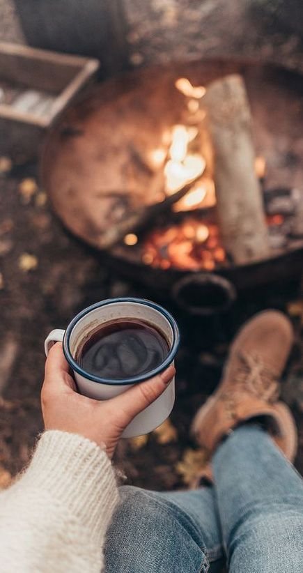 Femme au bord d'un feu de camp, tenant une tisane entre les mains
